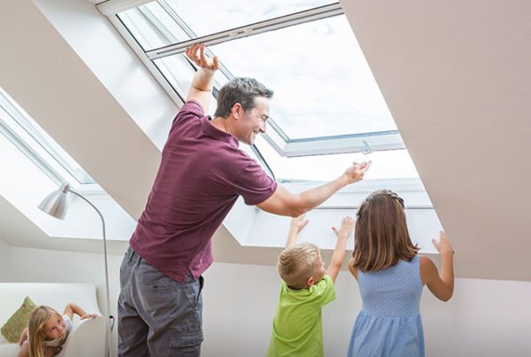 Vater öffnet mit seinen Kinder ein Rollo für Dachfenster