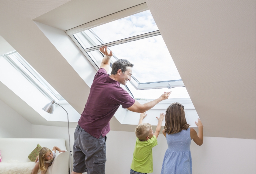 Person bedient ein Insektenschutz-Rollo am Dachfenster, Kinder schauen zu