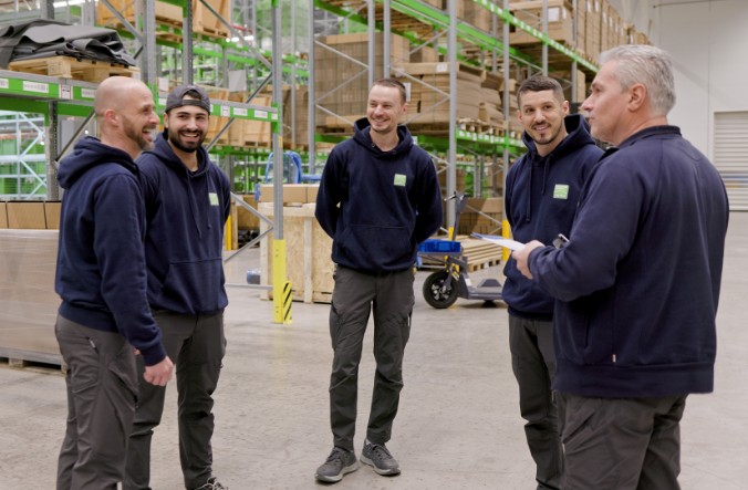 Team-Besprechung im Neher-Lager: Mitarbeitende im Austausch zwischen Regalen und Kommissionierbereich.