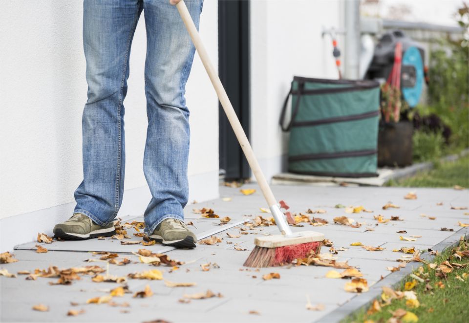 Person fegt Herbstlaub von der Terrasse; LISA Lichtschachtabdeckung verhindert, dass Laub in den Lichtschacht fällt.