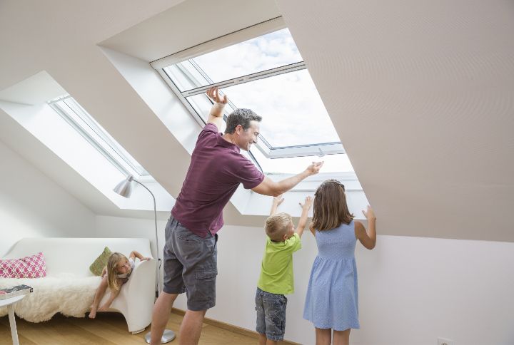 Familie bedient ein Fliegengitter-Rollo am Dachfenster im Dachgeschoss; leichte Handhabung, klare Sicht nach draußen.