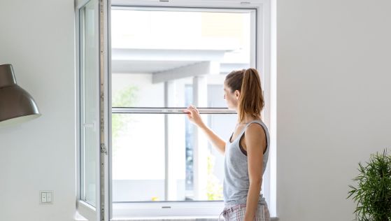 Eine Frau zieht ein Insektenschutz-Rollo an einem Fenster herunter, um Insekten aus dem Zuhause fern zu halten.
