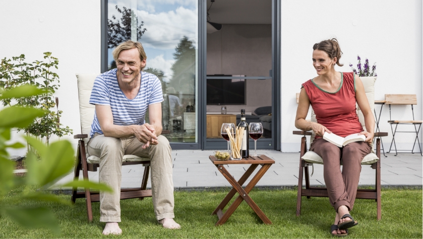 Paar sitzt im Garten und im Hintergrund ist die Insektenschutz Drehtür von Neher zu sehen.