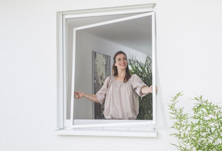 Frau hängt einen Neher Spannrahmen am Fenster ein; leichter Aluminiumrahmen mit Insektenschutzgewebe, einfache Handhabung beim Ein- und Aushängen.