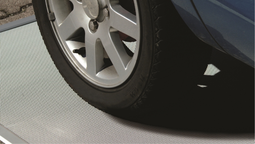 Nahaufnahme eines Autoreifens auf befahrbarem Streckmetall‑Gewebe einer Lichtschachtabdeckung.