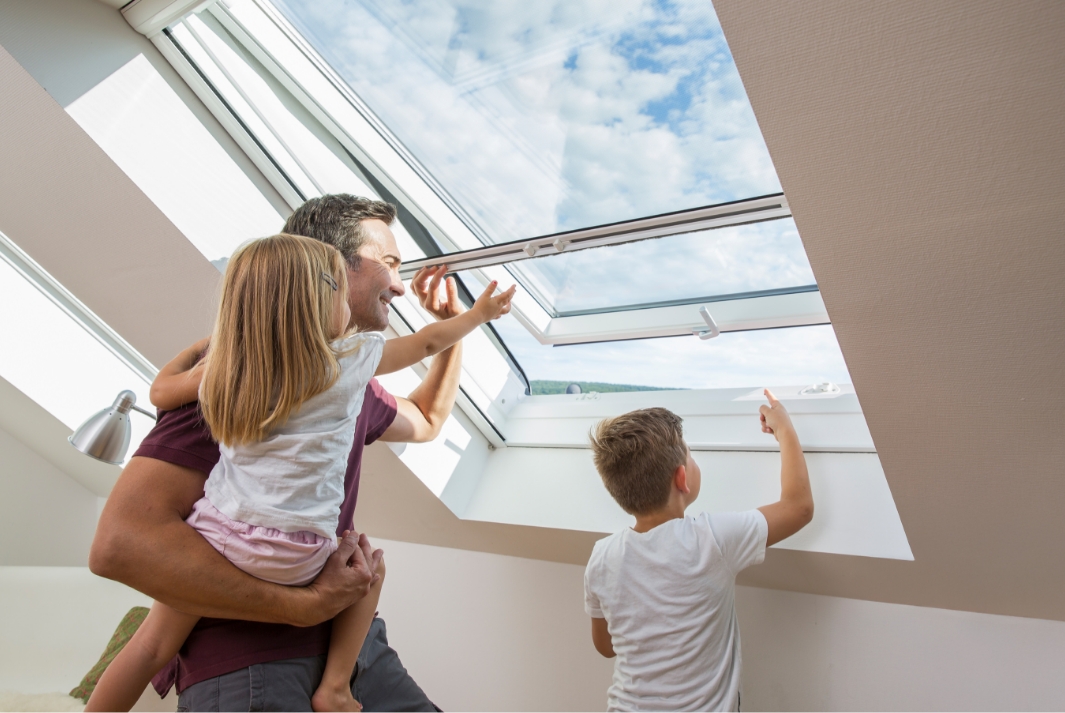 Person mit zwei Kindern öffnet Dachfenster mit installiertem Fliegengitter Rollo von Neher Insektenschutz.