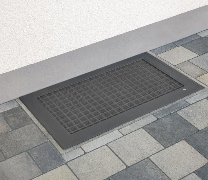 ELSA Lichtschachtabdeckung in Anthrazit, flächenbündig in einen gepflasterten Hof vor der Hauswand integriert.