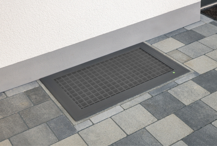 ELSA Lichtschachtabdeckung in Anthrazit bündig eingebaut auf einem gepflasterten Hof vor der Hauswand.
