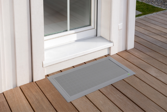 TERRESA Lichtschachtabdeckung von Neher bündig in eine Holzterrasse integriert, direkt vor der weißen Terrassentür.