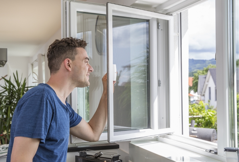 Person bedient Insektenschutz Pendelfenster und schaut nach außen.