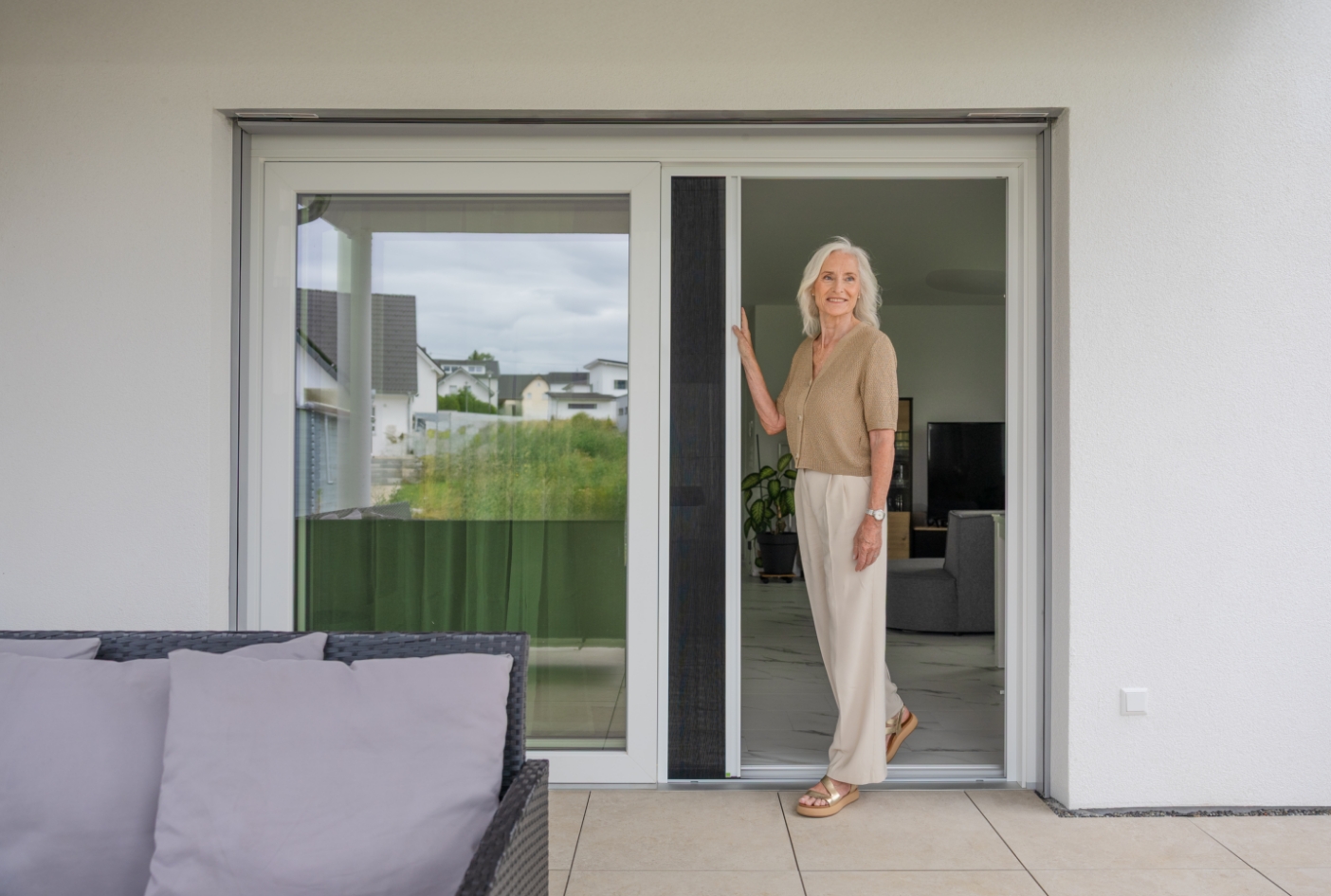 Person verschiebt ein weißes Neher Insektenschutz‑Plissee leicht und mühelos an einer großen Terrassen‑Schiebetür zur Seite.