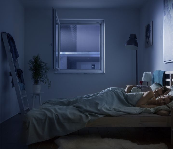Schlafzimmer mit geöffnetem Fenster in der Nacht. Ein Paar schläft ruhig, geschützt durch Neher Polltec Pollengewebe, das Pollen und Insekten draußen hält und frische Luft hereinlässt.