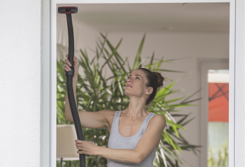 Frau reinigt ein eingesetztes Neher Insektenschutzgitter mit dem Staubsauger.