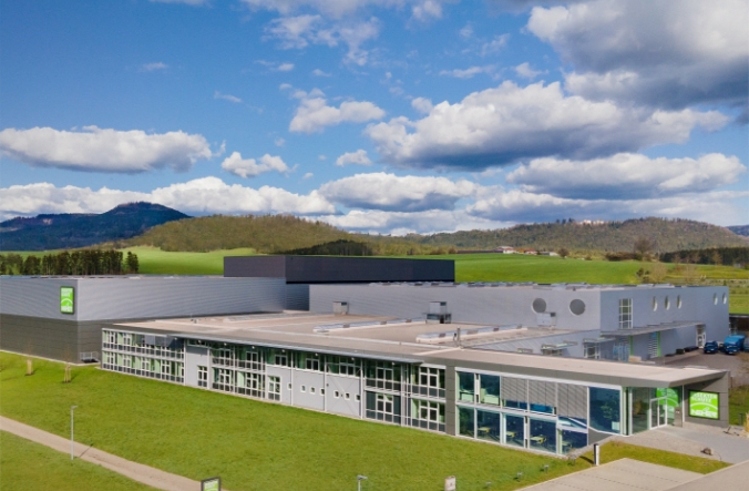 Neher company building with administration, warehouse and workshop in a modern, flat design, surrounded by green meadows under a blue sky.